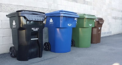 4 trash cans lined up along an outdoor wall